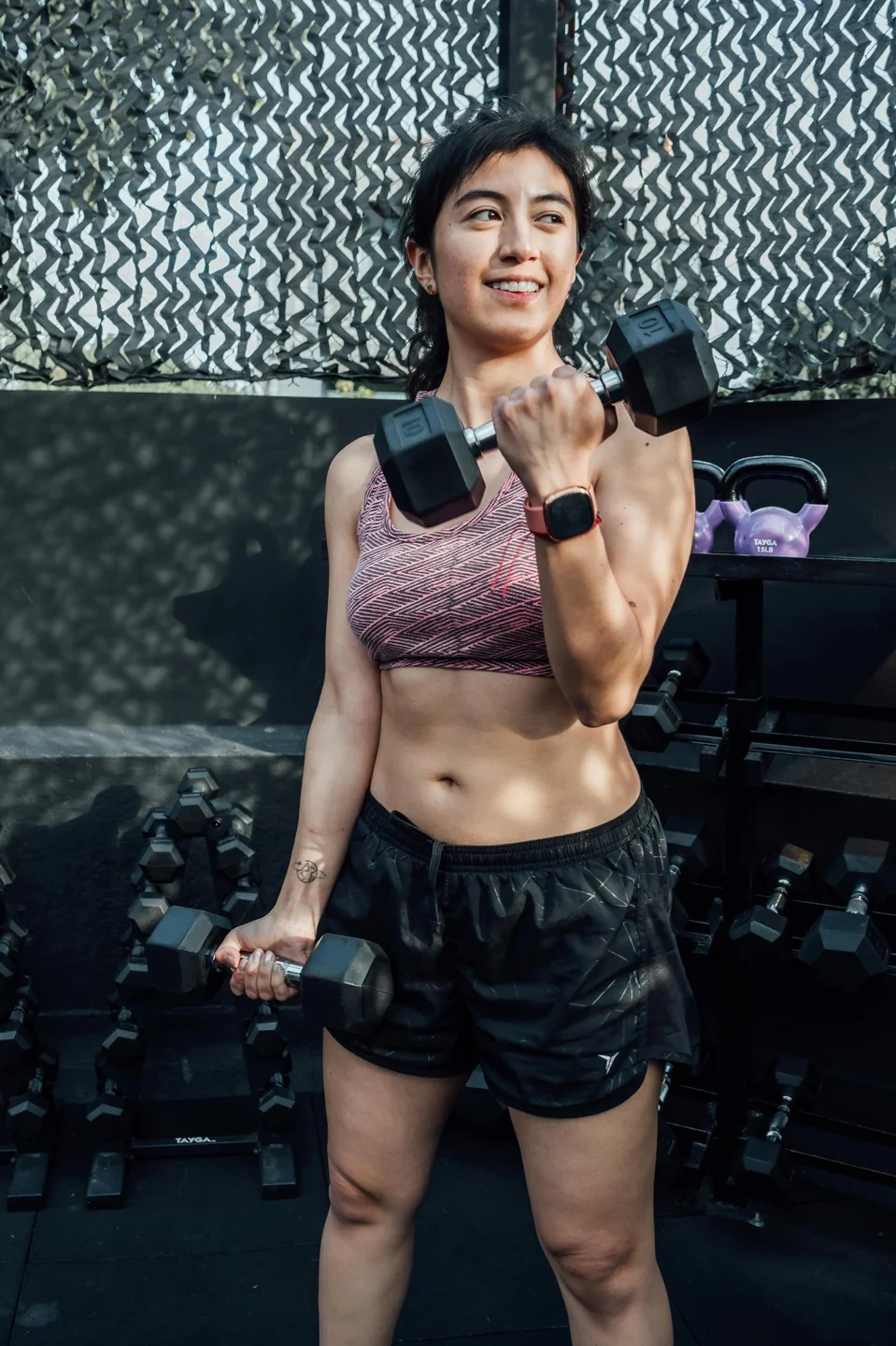 Una mujer haciendo curl con mancuernas en un gimnasio en casa, sonriendo