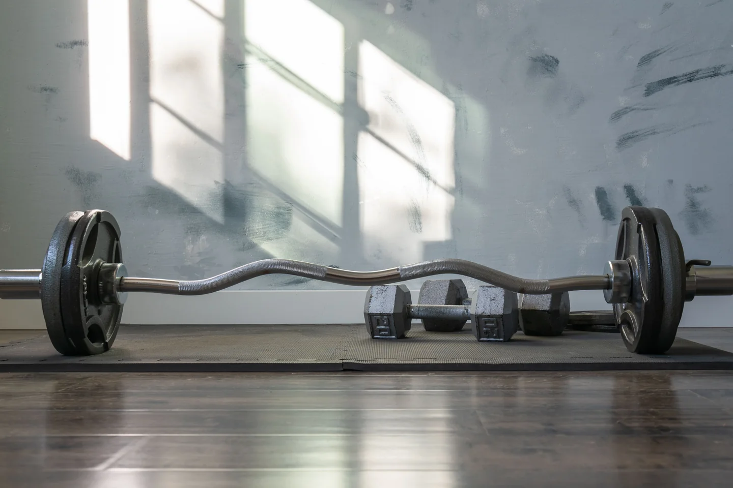 A barbell and a pair of dumbbells on a gym floor in natural light